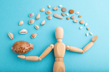 Wooden mannequin juggling sea shells on blue pastel background. close up