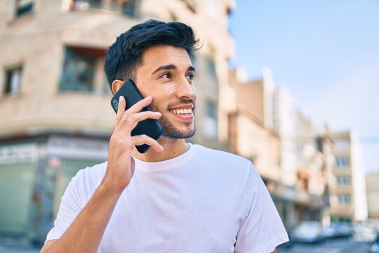 Young latin man smiling happy talking on the smartphone walking at the city.