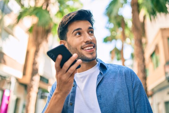 Young latin man smiling happy sending voice message using smartphone at the city.