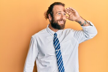 Handsome man with beard and long hair wearing business clothes very happy and smiling looking far away with hand over head. searching concept.