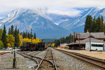 Railway tracks in small mountain town surrounded by massive mountains in the clouds on autumn day with colourful trees