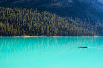 Solo canoe in empty turqouise blue glacial lake surrounded by natural wilderness forest and mountain