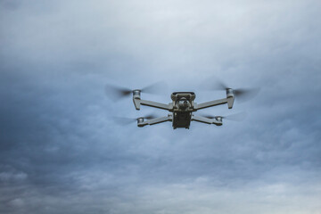 White drone hoovering in the midflight, photographed against the cloudy sky