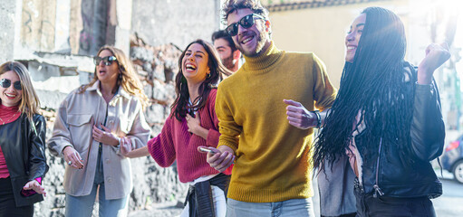 Group of young Friends gathering in the street listening music from smartphone and dancing together. Multiracial millennials having fun outdoors joking together. focus on the African descent woman. - obrazy, fototapety, plakaty