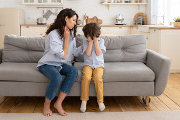 Caring mom supporting little preschool son. Beautiful female parent comfort crying offended kid. Small boy upset, stressed, abused or frightened with nervous supportive mother on couch in living room