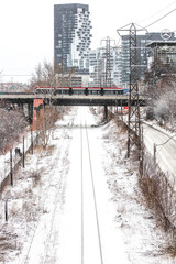 City railway tracks covered in snow in winter with LRT vehicle visible going over bridge