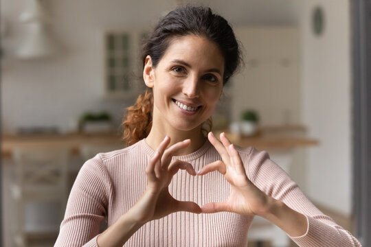 I love you. Grateful loving young latina female posing for portrait hold heart of united fingers close to breast. Happy hispanic woman look at camera show like gesture express gratitude appreciation