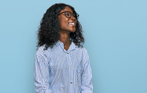 Beautiful african young woman wearing casual clothes and glasses looking away to side with smile on face, natural expression. laughing confident.
