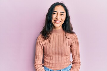 Hispanic teenager girl with dental braces wearing casual clothes looking positive and happy standing and smiling with a confident smile showing teeth