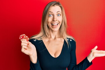 Beautiful caucasian woman playing poker holding casino chips celebrating achievement with happy smile and winner expression with raised hand