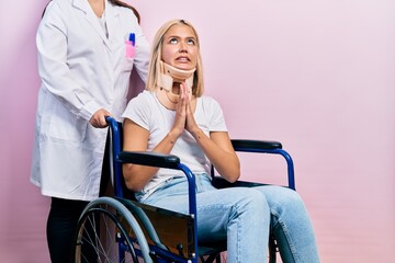 Beautiful blonde woman sitting on wheelchair with collar neck begging and praying with hands...