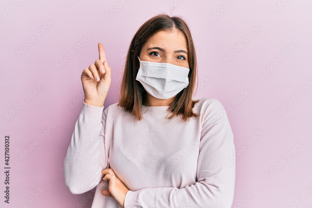 Sticker young beautiful woman wearing medical mask smiling with an idea or question pointing finger up with 