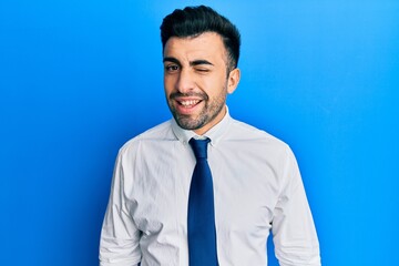 Young hispanic man wearing business clothes winking looking at the camera with sexy expression,...