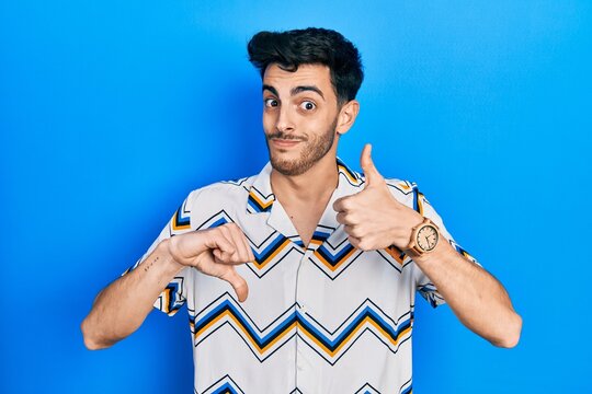 Young hispanic man wearing casual clothes doing thumbs up and down, disagreement and agreement expression. crazy conflict