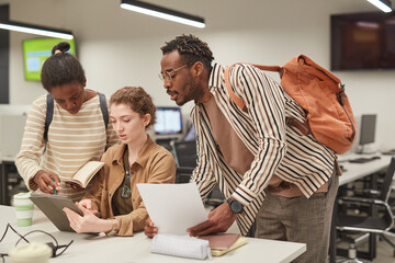 Diverse group of students working together in modern school library and using digital tablet