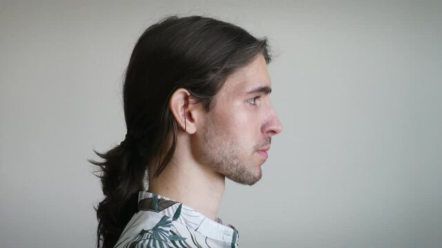 Young long-haired man drinking a glass of water, side view, loose ponytail, 4K face detail
