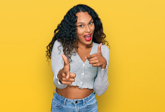 Young hispanic woman with curly hair wearing casual clothes pointing fingers to camera with happy and funny face. good energy and vibes.