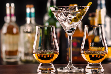 Expensive single malt whisky in tasting glasses and a cocktail martini with green olives served on ...