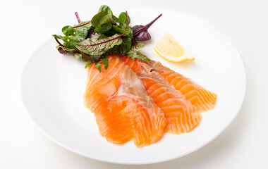 Salmon pieces on a white plate with basil leaves and lemon wedge 