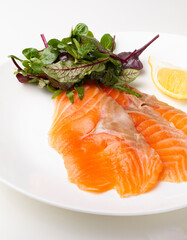 Salmon pieces on a white plate with basil leaves and lemon wedge 