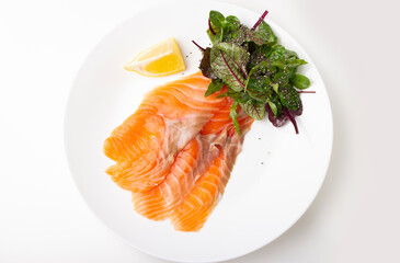 Salmon pieces on a white plate with basil leaves and lemon wedge 