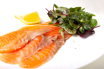 Salmon pieces on a white plate with basil leaves and lemon wedge 