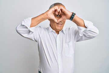 Handsome senior man wearing casual white shirt doing heart shape with hand and fingers smiling looking through sign