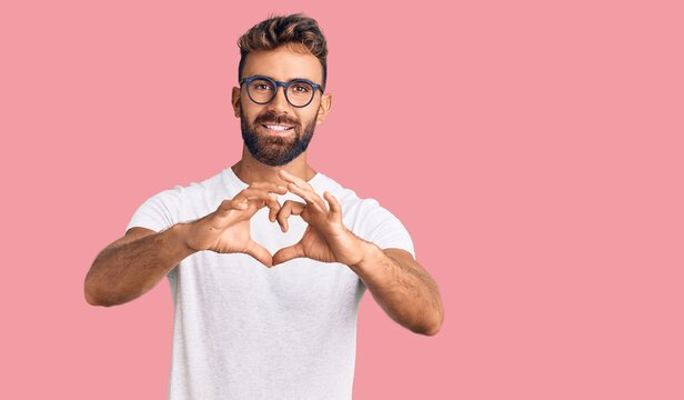 Young hispanic man wearing casual clothes and glasses smiling in love doing heart symbol shape with hands. romantic concept.
