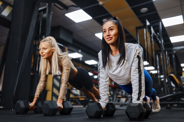 Fototapeta na wymiar Healthy lifestyle. Portrait of two young athletic girls doing plank in the gym.