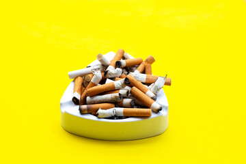 Ashtray and cigarettes on yellow background.