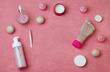 On the pink surface are candles, cream, sponges, foam, foot scrub, serum. Foot care, hygiene and foot hydration.Packaging of the cream in the form of a foot.Eyebrow Tweezers. Beauty accessories.