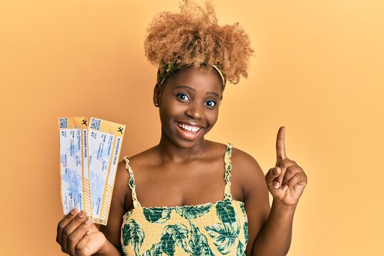 Young african woman with afro hair holding boarding pass smiling happy pointing with hand and finger to the side