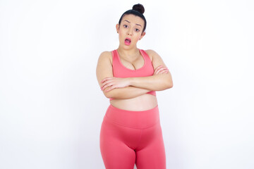 Shocked embarrassed young beautiful Arab pregnant woman in sports clothes against white wall keeps mouth widely opened. Hears unbelievable novelty stares in stupor