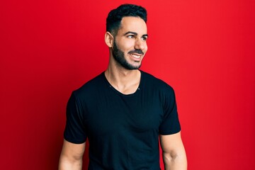 Young hispanic man wearing casual black t shirt looking to side, relax profile pose with natural face and confident smile.