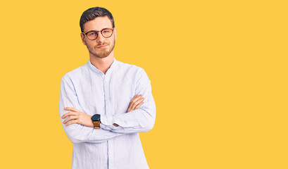 Handsome young man with bear wearing elegant business shirt and glasses skeptic and nervous, disapproving expression on face with crossed arms. negative person.