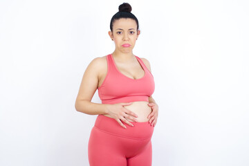 young beautiful Arab pregnant woman in sports clothes against white wall depressed and worry for distress, crying angry and afraid. Sad expression.