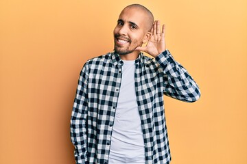 Hispanic adult man wearing casual clothes smiling with hand over ear listening and hearing to rumor or gossip. deafness concept.