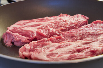 Red pork steaks with a fat layer in a frying pan.