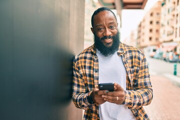 African american man with beard using smartphone typing and texting at the street with a happy smile