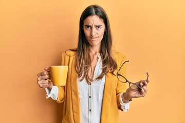 Young beautiful woman wearing business style drinking cup of coffee skeptic and nervous, frowning...