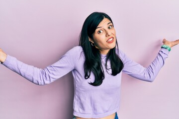 Young hispanic woman wearing casual clothes clueless and confused expression with arms and hands...