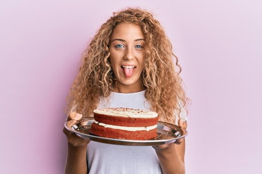 Beautiful caucasian teenager girl holding carrot cake sticking tongue out happy with funny expression.