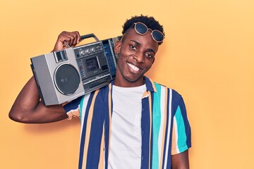 Young african american man holding boombox, listening to music looking positive and happy standing and smiling with a confident smile showing teeth