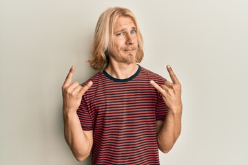 Caucasian young man with long hair doing rock gesture skeptic and nervous, frowning upset because...