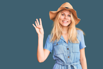 Obraz na płótnie Canvas Young beautiful blonde woman wearing summer hat and dress showing and pointing up with fingers number four while smiling confident and happy.