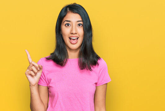 Beautiful asian young woman wearing casual pink t shirt pointing finger up with successful idea. exited and happy. number one.