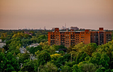 Fototapeta na wymiar The Toronto skyline is seen in the distance behind an apartment building set in a green urban forest at sunset in the summer