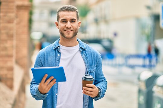 Young caucasian man smiling happy using touchpad and drinking coffee at the city.