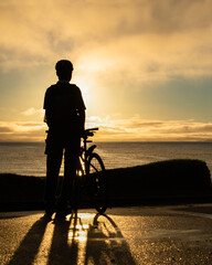 Obraz na płótnie Canvas Silhouette image of a cyclist watching the sunrise at Milford beach, Auckland. Vertical format.