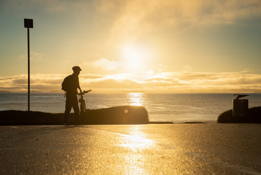 Silhouette image of a cyclist getting ready to ride on the beach at sunrise